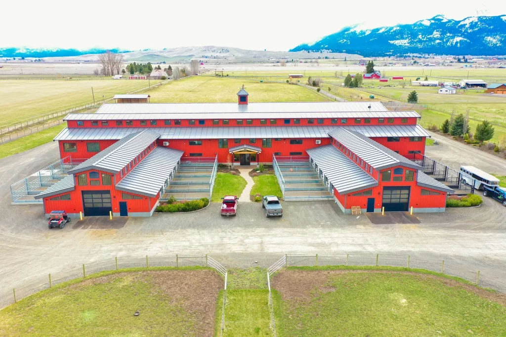 Exterior of Hot Property equine facility back of barn, showing indoor and outdoor stables, back entrance, parking areas, and spacious outdoor arenas.