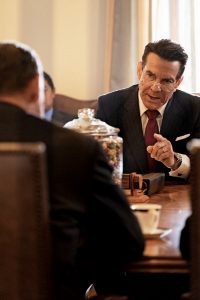 Dennis Quaid as Ronald Reagan in his film "Reagan", sitting in a conference. He is in mid speech and is pointing at the man in front of him in an accusatory manner.