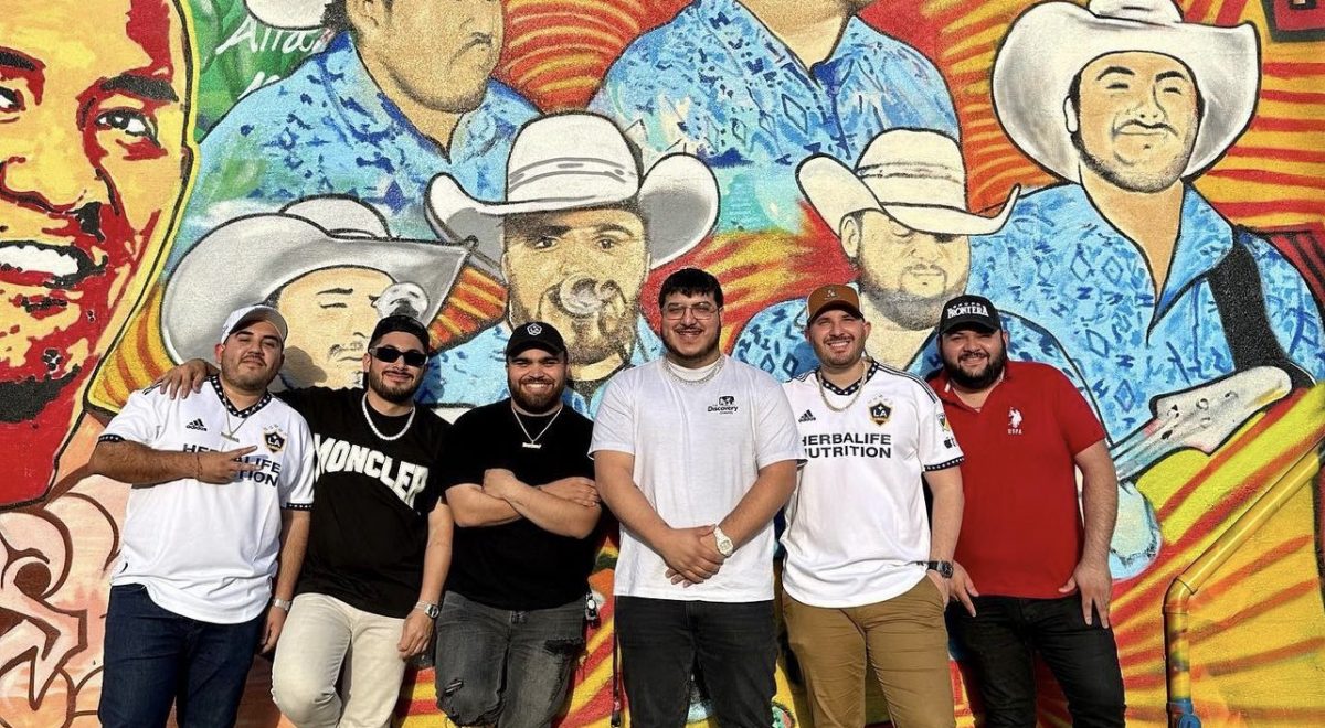 Members of Grupo Frontera stand in front of a mural.