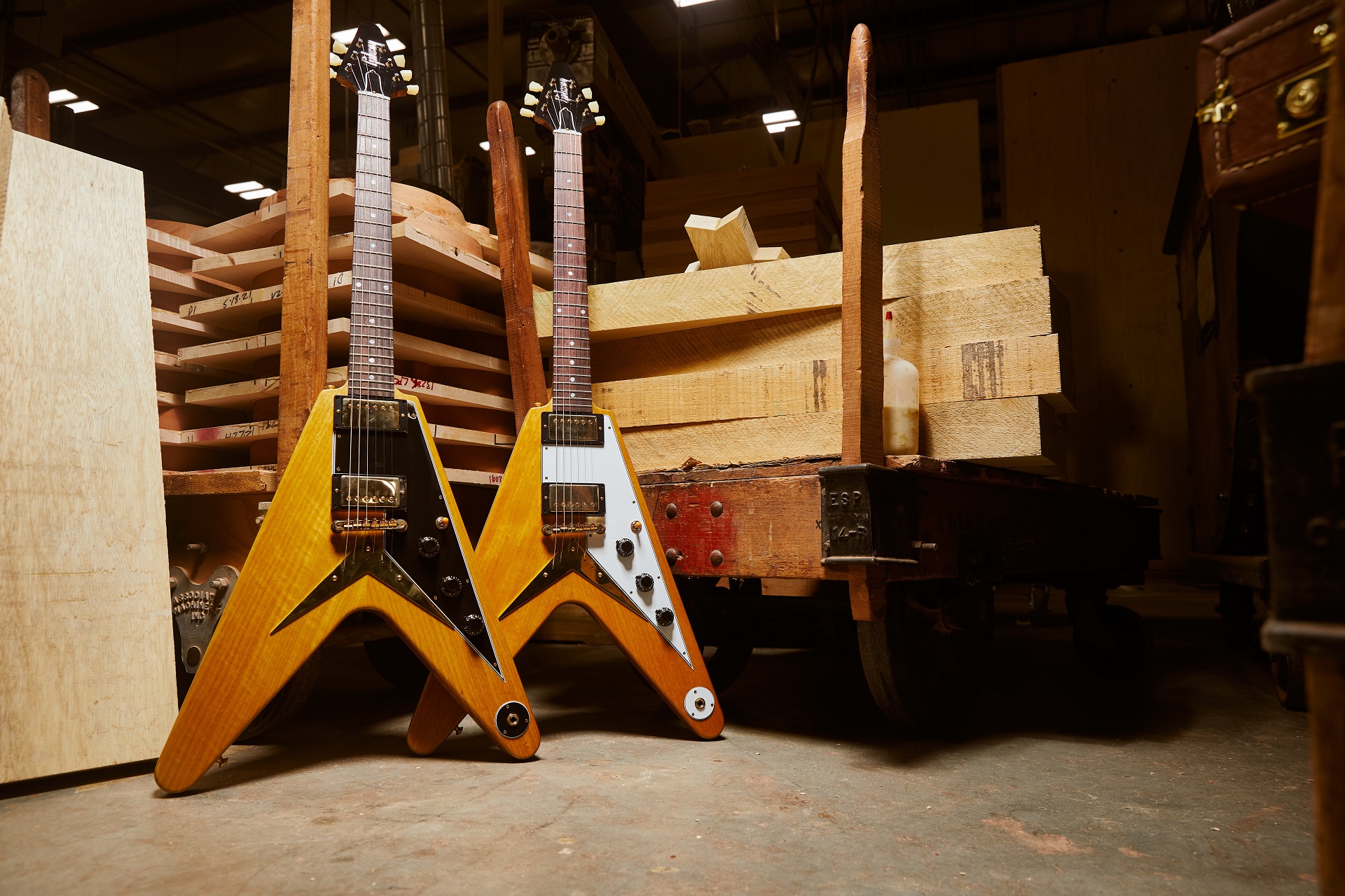 Two Gibson Custom Shop 1958 Korina Flying V Reissues (one in Black and White) behind the backdrop of a Gibson warehouse.