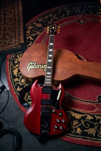 Gibson SG Standard 61 Faded Maestro Vibrola guitar in Vintage Cherry leaning against a brown leather Gibson guitar case.