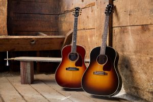 J-45 Deluxe in Rosewood Burst and J-45 Standard in Vintage Sunburst guitars leaning against a warehouse wall.