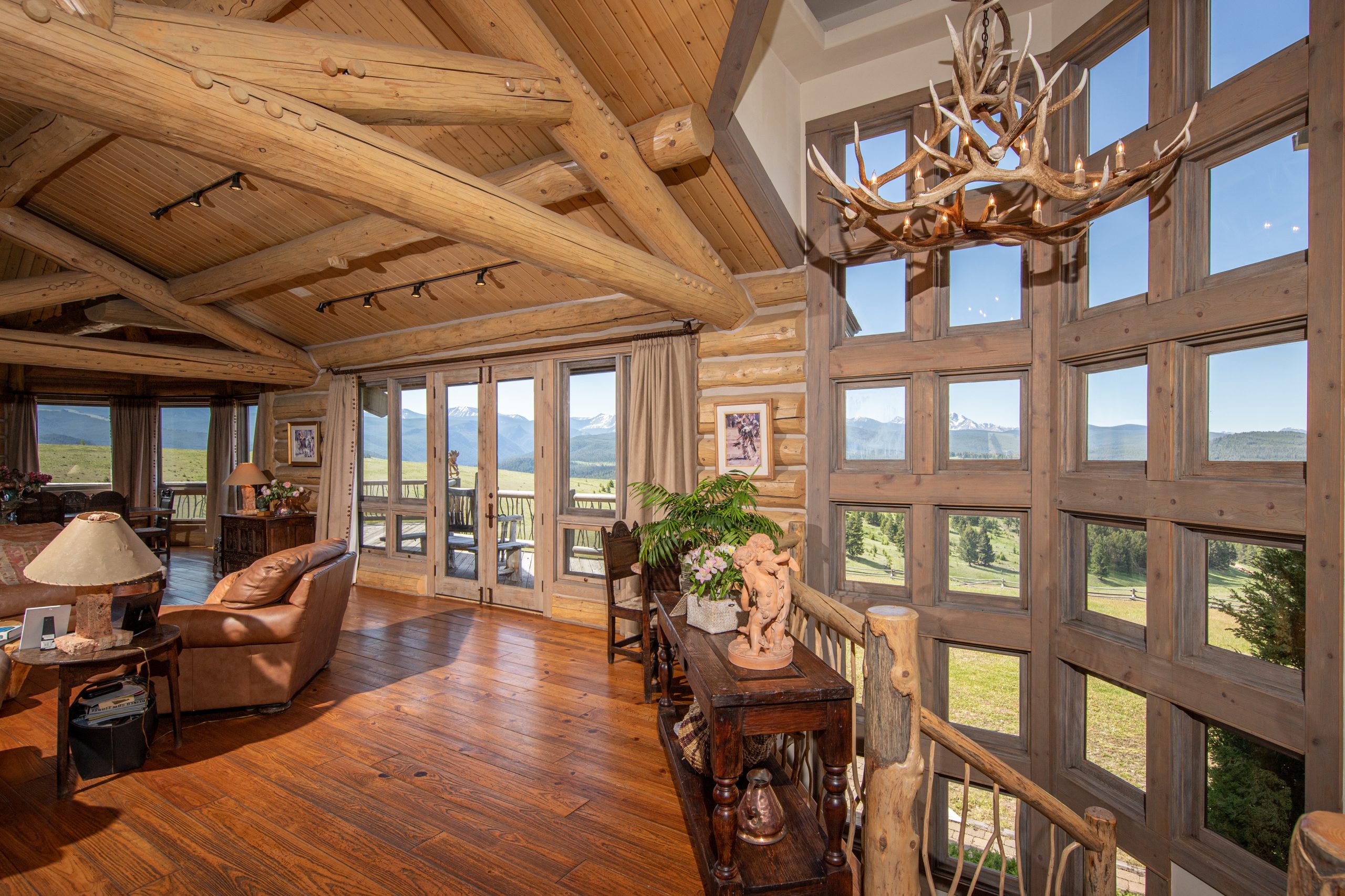 A view of the Montana mountains from the wood-paneled windows of Kokopelli Ranch's living room, furnished with a rustic style.