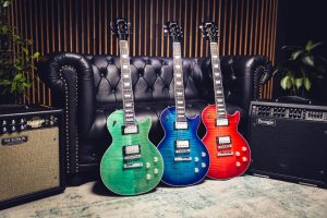 The Gibson LP Modern Figured guitar in green, blue, and red, leaning against a black leather couch in a recording studio.
