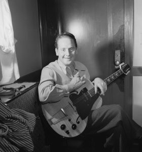 Les Paul sitting on a couch smiling with a Gibson guitar in his hands circa January 1947.