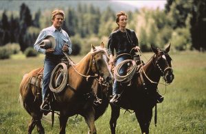 Actors Robert Redford and Kristen Scott Thomas ride horses across a pasture in the 1998 film "The Horse Whisperer."