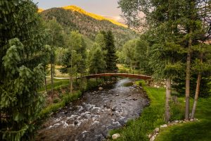 A view of the property's bridge crossing the river with the Colorado mountains in the background.
