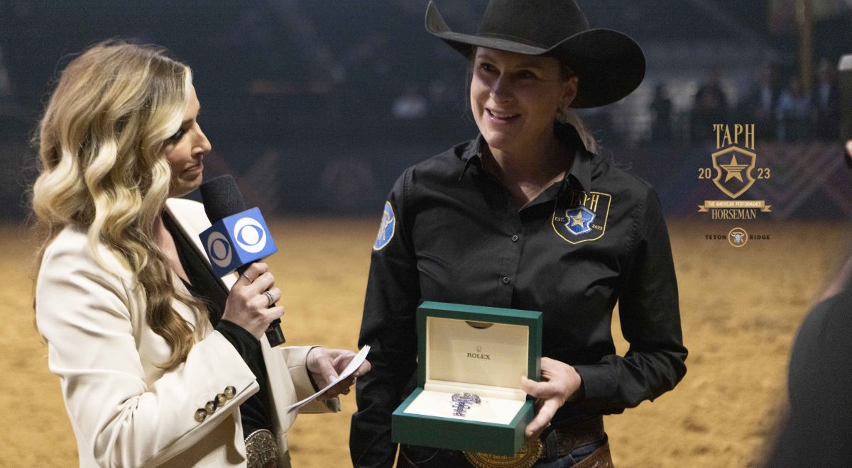 Sarah Dawson is interviewed by a journalist in the Globe Life Field arena as she holds a Rolex watch gifted to her for her win at the 2023 American Performance Horseman.