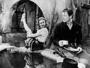 Actress Dorothy Malone lifts her leg in a comical pose meant to be seductive next to actor Joel McCrea in the 1949 film "Colorado Territory."