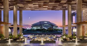 The AT&T stadium in full view from the back patio of the Texas Live! luxury hotel, which has decorative water fountains and multiple lounge areas.