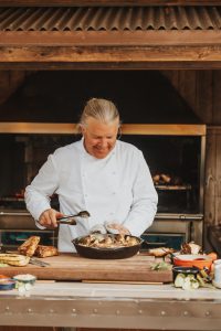 Chef Joshua Drage uses tongs to prepare a cast-iron skillet dish in his kitchen.
