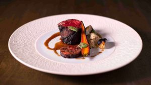 A small piece of rare wagyu beef garnished with brown sauce from the Brush Creek Ranch menu on a white plate.