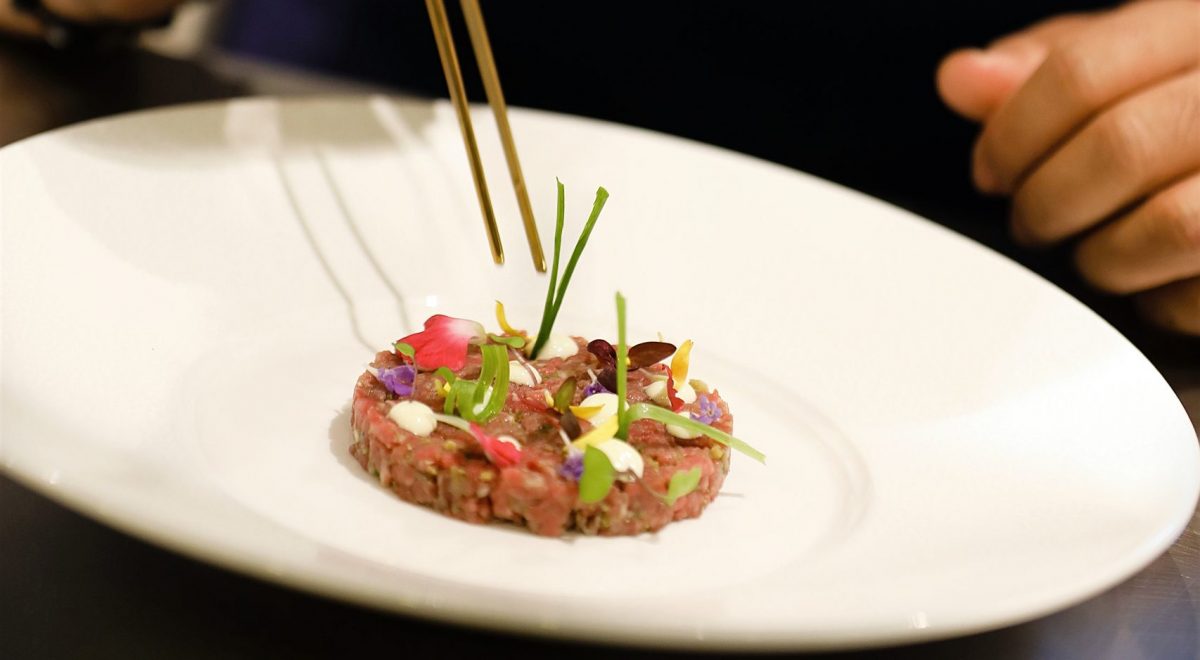 A chef uses cooking pliers to delicately place garnish onto a wagyu tartare at the Brush Creek Ranch restaurant.