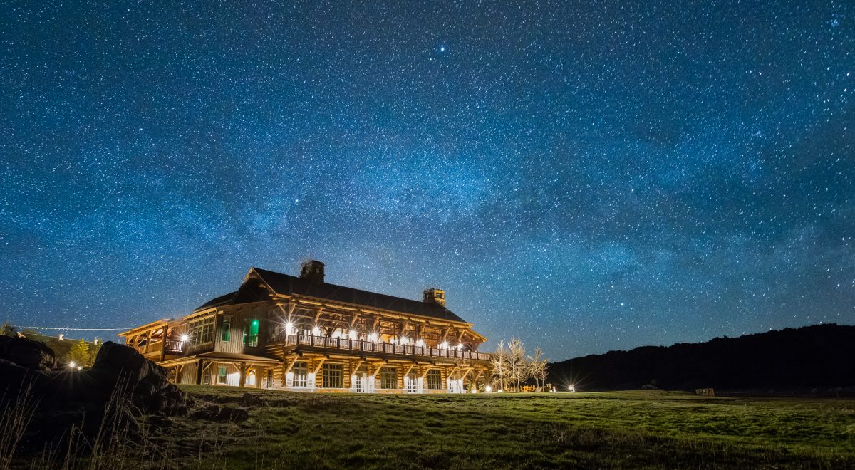 The Brush Creek Ranch lodge — an illustrious well-lit log cabin — sits against a sky full of stars.