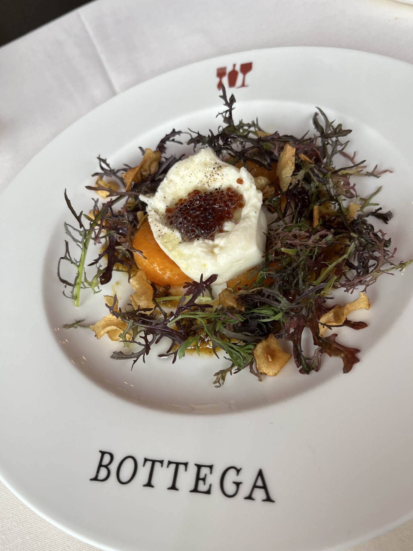 A creamy white entree dish placed on top of a leafy garnish sits on a white plate with the word "BOTTEGA" in black letters on the rim.
