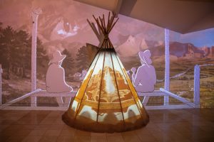A "Find Your West" exhibit art piece, featuring a tepee glowing with projections on and behind it.