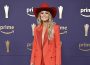 Lainey Wilson smiles on the ACM Awards 2024 red carpet wearing a red pantsuit and red cowgirl hat.