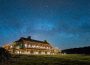 The Brush Creek Ranch lodge — an illustrious well-lit log cabin — sits against a sky full of stars.